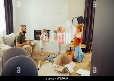 Unpacking boxes. Nice positive man looking at his family while holding some books in his hands Stock Photo