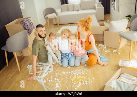 Home sweet home. Delighted nice family sitting together on the floor in the living room while being happy about their new house Stock Photo