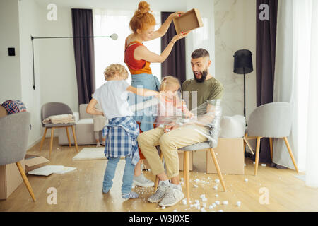 Fun games. Nice happy kids having fun while tying up their father to the chair Stock Photo