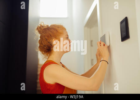 Security system. Serious young woman standing near the control panel while setting up the alarm system Stock Photo