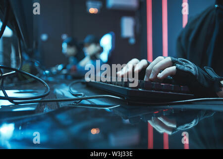 Close-up of unrecognizable computer engineer in fingerless gloves sitting at table and typing on keyboard Stock Photo