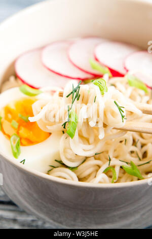 Instant noodles on wooden background. Cooked chinese instant noodles. Soup Ramen with egg and radish Stock Photo