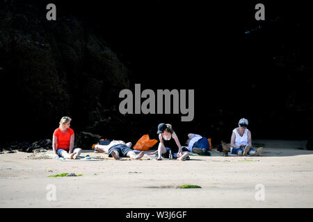 Sunbathers sit in front of a shady cliff during the hot sunshine on Towan beach in Newquay, Cornwall, the week before school holidays, as more hot weather is due to hit the UK this week. Stock Photo