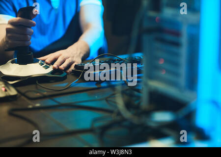 Close-up of unrecognizable gamer sitting at table with computer and cables and using 3D joystick Stock Photo