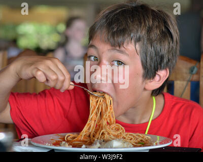 Cute little Canadian boy of mixed-race origin (Caucasian and Southeast Asian) digs into a plate of spaghetti. Stock Photo