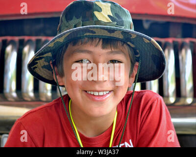 Cute Canadian boy of mixed race (Caucasian and Southeast Asian) smiles for the camera in front of an American vintage car. Stock Photo