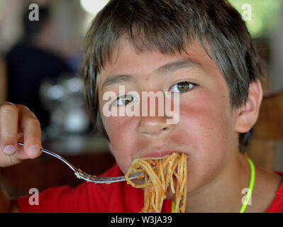 Cute Canadian mixed race boy eats pasta. Stock Photo