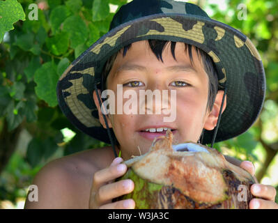 Cute Canadian mixed race boy (Caucasian and Southeast Asian) on vacation in Cuba holds a fresh coconut with both hands. Stock Photo