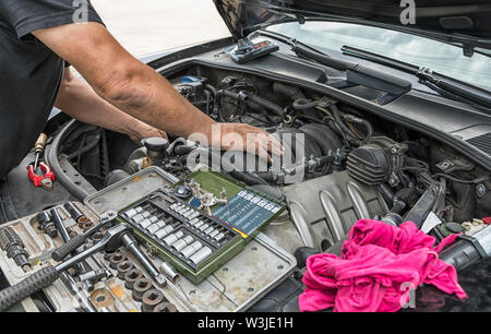 Two hands carry out repairs in the engine compartment of a car. Stock Photo