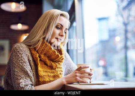 Beautiful young woman in a cafe drinking coffee and using her phone Stock Photo