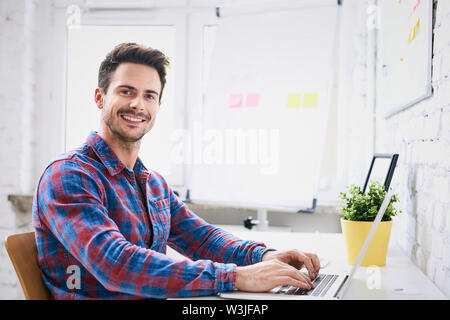 Succesful young web designer, programmer working on laptop in start-up office Stock Photo