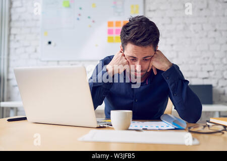 Depressed young man looking on financial documents working at office Stock Photo