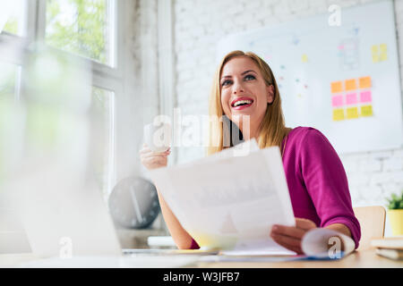 Smiling woman working at office, drinking coffee and browsing documents Stock Photo