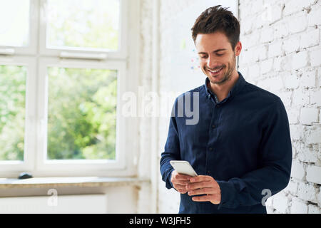 Happy young man using his smartphone at office Stock Photo