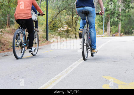 people, leisure and lifestyle concept - happy young couple riding bicycles along road in summer - Image Stock Photo
