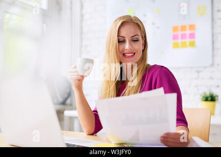Beautiful young businesswoman drinking coffee and looking through documents Stock Photo