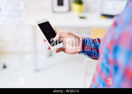 Closeup of young male hand holding phone touching screen in modern office Stock Photo
