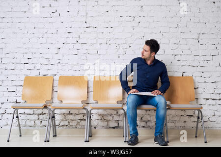 Awaiting his turn. Handsome casually dressed young man waiting for job interview in modern office building Stock Photo