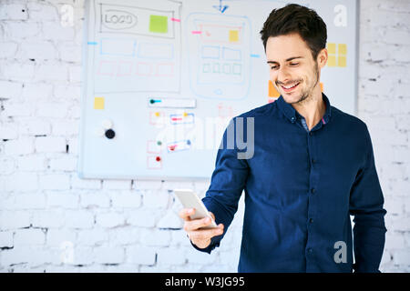 Web developer standing in front of whiteboard with website wireframe and looking at phone Stock Photo