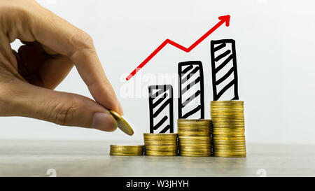 Long-term investment or making money with the right concepts. A business man putting coin on stack of coins on a table with growing graph on coins pil Stock Photo