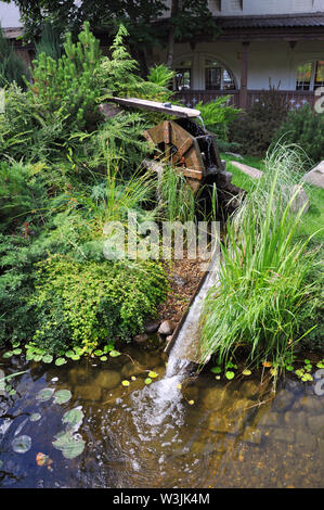 Landscape and arrangement. Driving mill wheel with falling water in the garden. Stock Photo