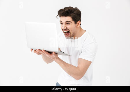 Image of shocked screaming young man posing isolated over white wall using laptop computer. Stock Photo