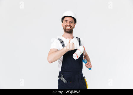 Portrait of a handsome bearded builder man wearing overalls standing isolated over white background, holding paint brush Stock Photo