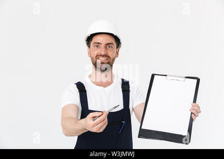 Confident bearded builder man wearing overalls and hardhat standing isolated over white background, showing blank tablet Stock Photo