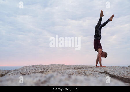 Man doing a hand stand while practicing yoga at dusk Stock Photo
