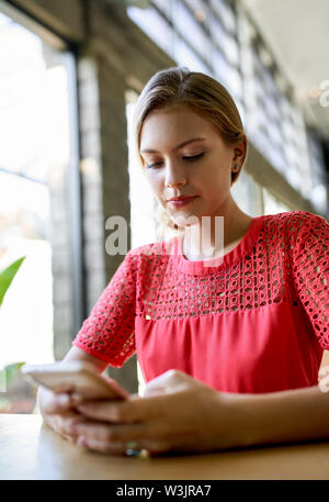 Closeup lifestyle portrait of young blonde caucasian natural millennial woman working on cellphone at modern tropical and bright office with plants Stock Photo