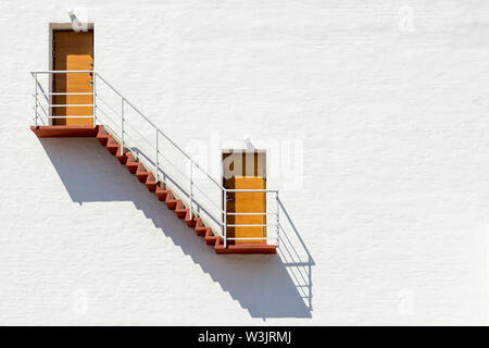 Two doors on a bright white wall connected by red stairs Stock Photo