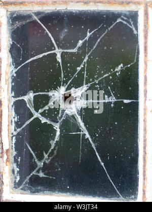 A bullet hole in a pane of old, dirty glass in an abandoned and derelict warehouse Stock Photo