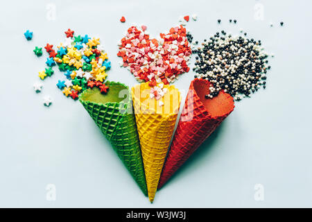 Small caramels of different shapes and colors are scattered on the surface of wafer cones. Pastry background with a variety of sweets Stock Photo