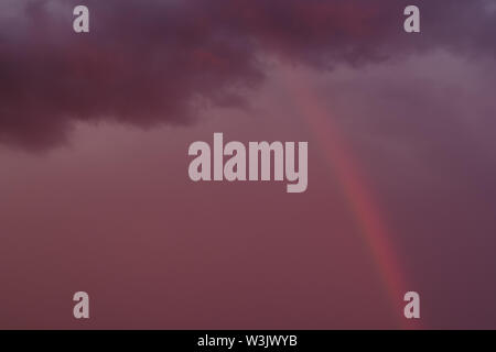 Full frame nature cloudy sky background with rainbow during rainy weather, pink purple bright vibrant colors Stock Photo