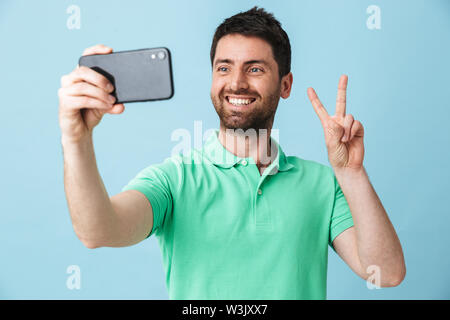 Portrait of a handsome bearded man wearing casual clothing standing isolated over blue background, taking a selfie Stock Photo
