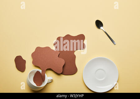 top view of paper cut coffee spills near white cup, saucer and spoon on beige background Stock Photo