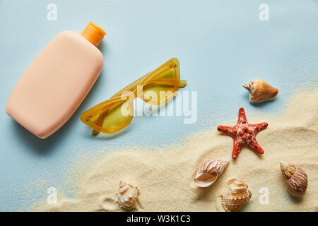 top view of sunscreen in bottle near seashells, starfish, sand and sunglasses on blue background Stock Photo