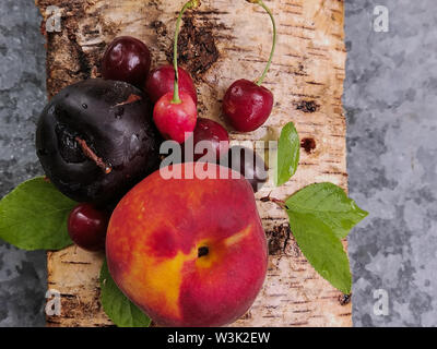 juicy fruits: peach, cherry and plum on the bark of birch trees in a summer day. summer freshness. Stock Photo