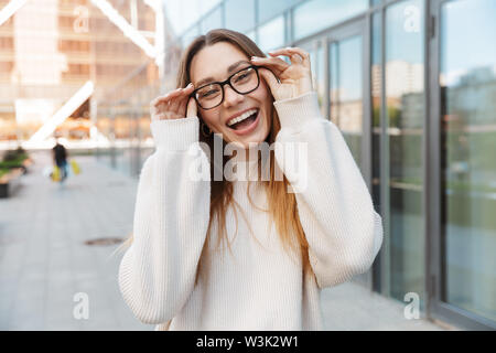 Image of a beautiful young happy excited business woman posing walking outdoors near business center wearing eyeglasses. Stock Photo