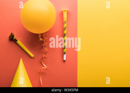 Top view of yellow balloon, streamer, party hat on coral and yellow background Stock Photo