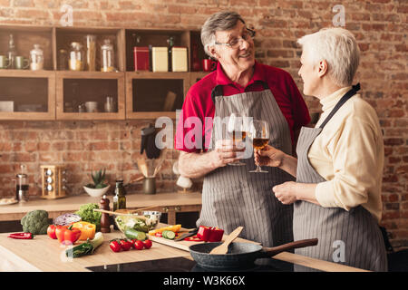 Laughing affectionate retired couple drinking wine together in kitchen Stock Photo