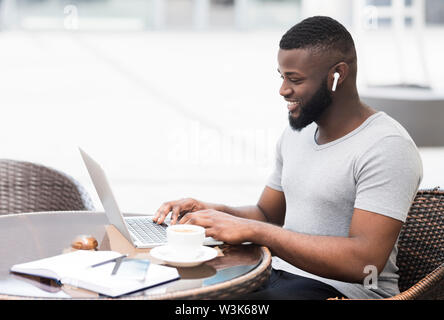 African guy using laptop, smiling and drinking morning coffee Stock Photo