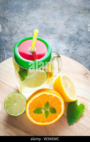 Jar of lemonade made of lemon, lime, orange and mint with a closed lid and a tube in it against background concrete floor. Stock Photo