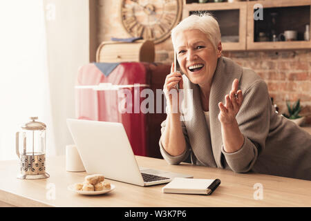 Active senior woman making order by phone in kitchen Stock Photo