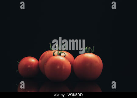 Fresh four tomato on a black glass table and dark background. Stock Photo
