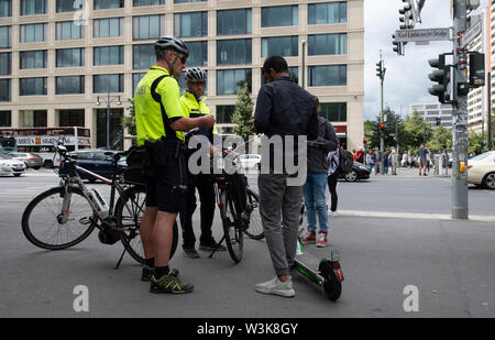 16 July 2019, Berlin: Police officers of the bicycle squadron check two youths with electric scooters on a sidewalk. Photo: Paul Zinken/dpa Stock Photo