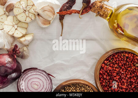 top view of garlic cloves, red onion, coriander and pink peppercorn in bowls on white paper background Stock Photo