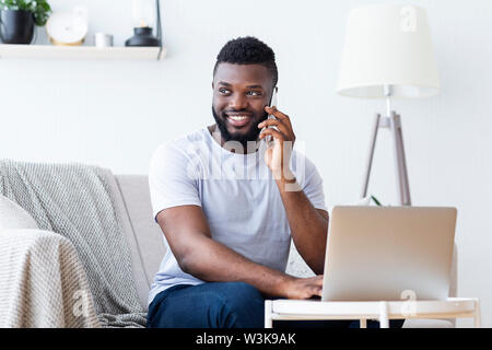 Cheerful man talking on phone and using laptop Stock Photo