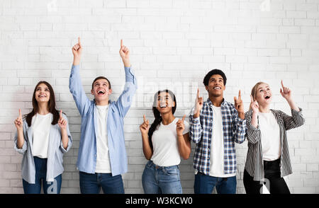 Teens pointing up on free space over white brick wall Stock Photo