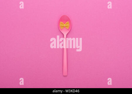 uncooked farfalle pasta on plastic spoon bowl isolated on pink Stock Photo